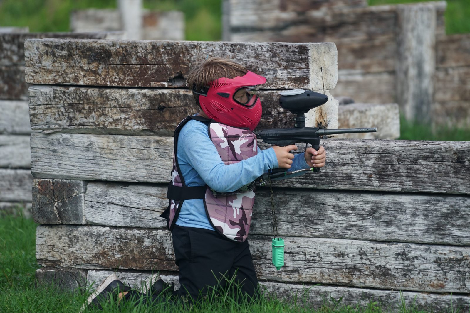 Young paintball player aiming from a wooden bunker at Fort Myers Paintball Park